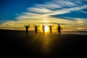 Five people on beach jumping up with sun setting