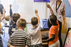 Several children raising their hands in a classroom Proposal writer