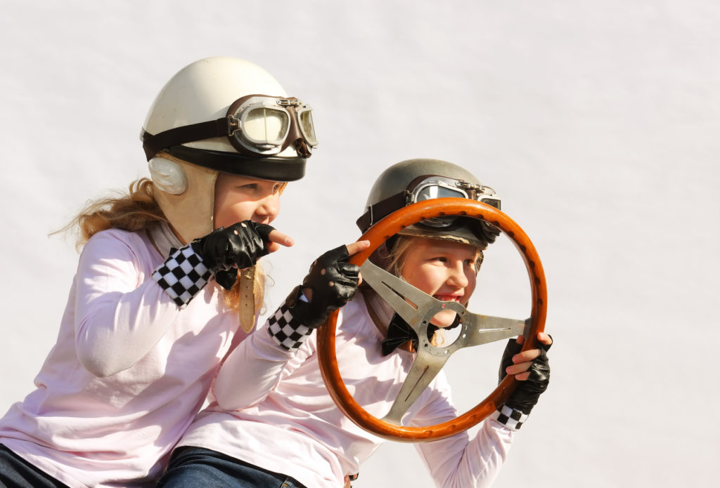 Two kids with helmets on playing with steering wheel