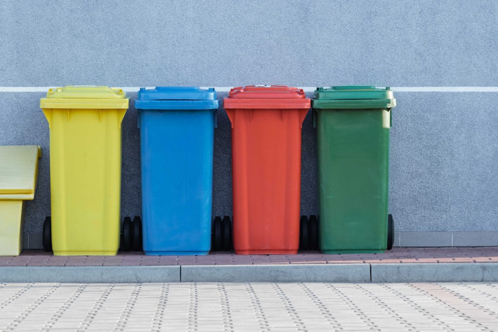Picture of yellow, blue, red, and green trash cans lined up against gray wall. Placer County California