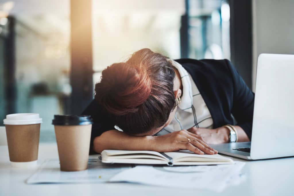 Lady with her head down on book with two coffees and a laptop.