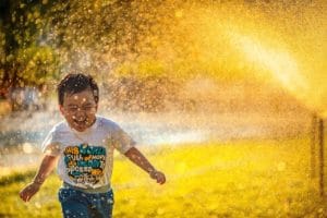 Child running through water sprinkler Finding joy