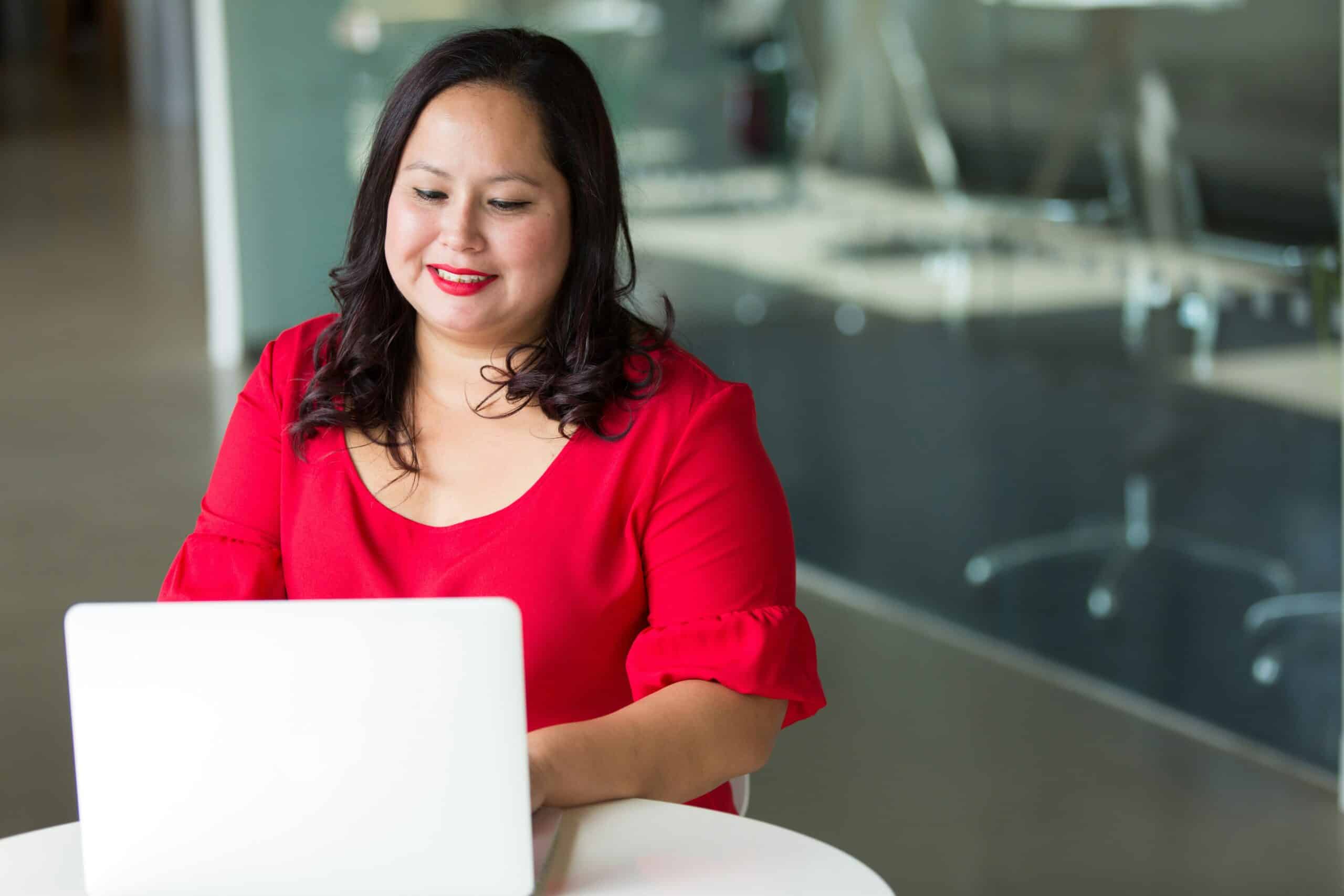 Female-presenting employee in bright red shirt working at laptop competitive edge